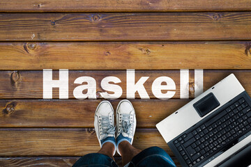 Wall Mural - Legs in sneakers standing next to laptop and Haskell on wooden floor. Haskell programming language.
