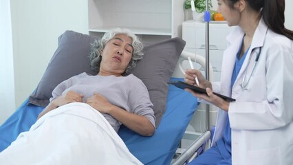 Wall Mural - Elderly Asian woman lying in hospital bed looking unwell, with young Asian doctor take a history of illness Health check and encouragement.