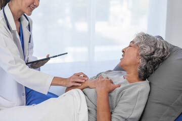 Wall Mural - Elderly Asian woman lying in hospital bed looking unwell, with young Asian doctor take a history of illness Health check and encouragement.