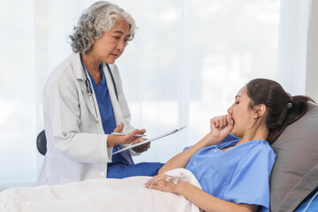 Wall Mural - An elderly Asian doctor with a stethoscope is checking young Asian patient in hospital bed, take history of illness Health check and encouragement