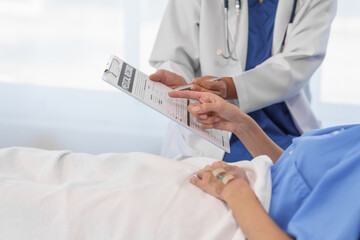 Wall Mural - An elderly Asian doctor with a stethoscope is checking young Asian patient in hospital bed, take history of illness Health check and encouragement