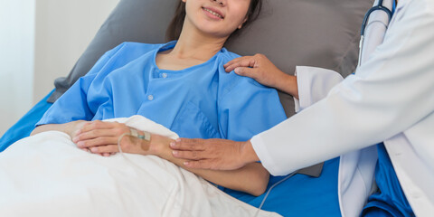 Wall Mural - An elderly Asian doctor with a stethoscope is checking young Asian patient in hospital bed, take history of illness Health check and encouragement