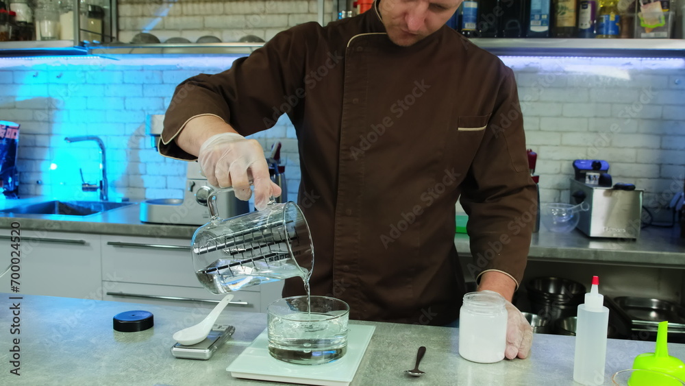 Chef pours liquid in glass from measure cup at table. Skilfully ...