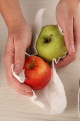 Wall Mural - Woman wiping apples with paper towel at light wooden table, top view