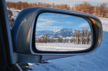 reflection of winter landscape with Tien Shan mountains and trees in field in snow in rearview mirror of the car. Concept of festive winter travel in Kazakhstan