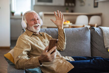 Phone, Senior Man And Watch Music Video, Streaming Podcast And Reading Happy Story, News Article Or Retirement Blog. Home, Smartphone And Elderly Person With Headphones, Relax And Listening To Song.