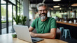 © Studio Nova - Cheerful man with a beard and glasses working on a laptop at a wooden desk