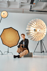 joyous attractive woman in casual attire posing with her photography equipment in her studio