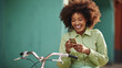 Young woman with curly brown hair, standing by a bicycle, looking at her smartphone