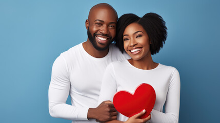 Smiling couple in white shirts, holding red heart-shaped objects, symbolizing love and togetherness.