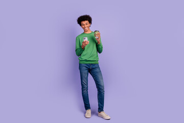 Poster - Full length photo of positive cheerful man dressed green sweater drinking tea typing modern device empty space isolated violet color background