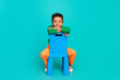 Photo of charming adorable boy wear stylish green clothes sitting little chair isolated on cyan color background