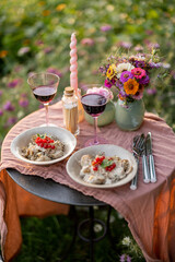 Table served with meals and wine for two on a flower lawn outdoors. Romantic dinner concept