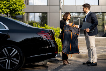 Female chauffeur gives a businessman his suit, after a business trip in luxury taxi. Concept of personal assistant, driver and business transportation service