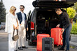Business couple standing by a minivan taxi waiting for their chauffeur or porter to help them with a suitcases. Concept of business trips and travel