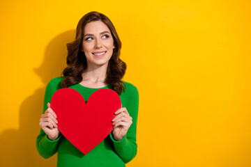 Poster - Photo of lovely cute woman dressed green stylish clothes hands hold red paper card look up empty space isolated on yellow color background