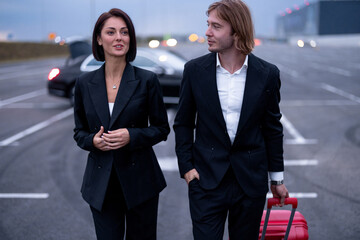 Wall Mural - Business couple walking with a suitcase on parking lot, arrived by luxury taxi. Concept of transportation and business trips