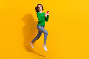 Sticker - Full body length photo of cheerful young energetic lady green pullover jeans addicted using cellphone isolated on yellow color background