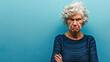 80 year old caucasian female with angry facial expression crossed arms on blue background with copy space