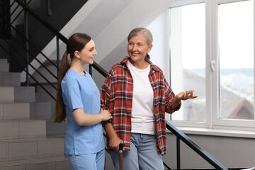 Sticker - Young healthcare worker assisting senior woman on stairs indoors