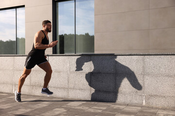 Canvas Print - Young man running near building outdoors. Space for text