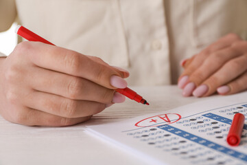 Wall Mural - School grade. Teacher writing letter A with plus symbol on answer sheet at white table, closeup