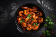 A spicy shrimp with herbs and red chili peppers in a black bowl, ready to be served.