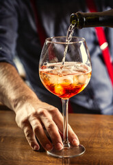 Canvas Print - The bartender at the bar prepares the summer cocktail Spritz Veneziano, pours Prosecco into a glass with ice