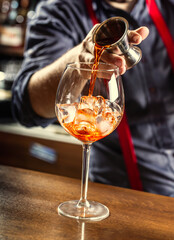 Wall Mural - The barman in the bar prepares a summer cocktail Spritz Veneziano, pours Aperol liqueur into a glass with ice