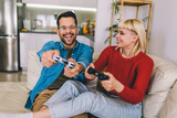 Fototapeta Londyn - Boyfriend and girlfriend playing video game with joysticks in living room. Loving couple are playing video games at home.