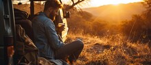 A Cheerful Man In A Denim Jacket Is Sitting In The Car Truck Checking A Phone And Drinking A Hot Drink In Nature During The Sunset. Creative Banner. Copyspace Image