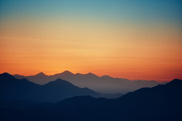 Poster - A stylized graphic depiction of a mountainous horizon at dusk, with silhouetted peaks and a gradient sky transitioning from warm oranges to cool blues.