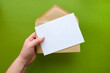 © tiena - A hand holds a envelope with a blank sheet of paper. Letter template on green background