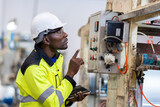 Fototapeta  - African male engineer department head Point to the electronic circuit board. of machinery in plastic and steel industries Wear a safety helmet and vest. holding laptop to work