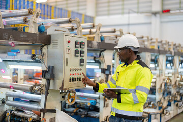 Wall Mural - African male engineer Pressing buttons on electronic circuit boards, machinery of plastic and steel industries. Use a laptop to check company business systems. Wear a safety vest and helmet.