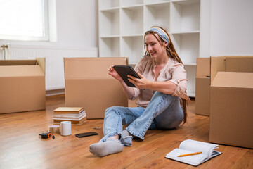 Wall Mural - Modern ginger woman with braids using digital tablet while moving into new apartment.	