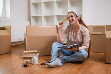 Wall Mural - Modern ginger woman with braids writing in notebook while moving in new home.	