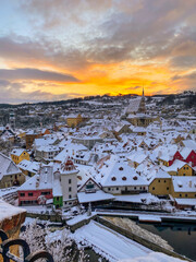 Wall Mural - Winter view of Czech Krumlov. Český Krumlov, UNESCO. Historical town with Castle and Church at sunrise. Beautiful winter morning landscape with an illuminated monument. Snowy cityscape scene from the 