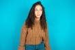Beautiful teen girl wearing knitted sweater over blue background 9LKstares aside with wondered expression has speechless expression. Embarrassed model looks in surprise