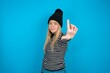 Teen caucasian girl wearing striped sweater and woolly hat making fun of people with fingers on forehead doing loser gesture mocking and insulting.