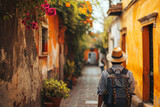 Fototapeta Fototapeta uliczki - Un homme avec un sac à dos en vacances dans une petite rue colorée d'une ville étrangère. Touriste en voyage, marche, découverte, visite, backpacker. Pour conception et création graphique.