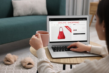 Woman with cup of tea shopping online during sale on laptop at home, closeup
