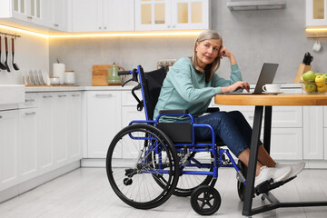 Wall Mural - Woman in wheelchair using laptop at table in home office