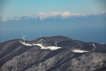 A distant view of a wind turbine on a snow-capped mountain peak of Taegi Mountain in Hoengseong County, Gangwon Province, South Korea.