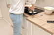 Woman putting pancakes on a frying pan in the kitchen at home.
