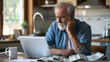 a Retired senior man Facing Financial Challenges: Serious Expression While Reviewing debt Bills and Laptop Indoors. Tax issues, mortgage, foreclosure, penalties and late fees concept