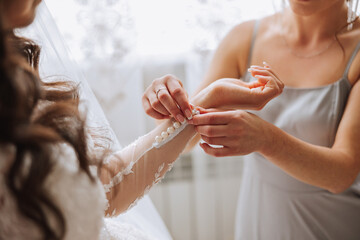 Morning of the bride. The bride's maid of honor helps the bride lace up her dress, fasten buttons on the dress or sleeves. Girlfriends help the bride fasten her dress