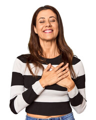 Elegant middle-aged Caucasian woman in studio setting laughing keeping hands on heart, concept of happiness.