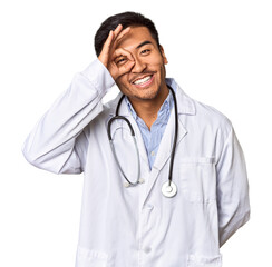 Wall Mural - Young Chinese man as a medical doctor in studio excited keeping ok gesture on eye.