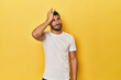 Young Hispanic man on yellow background forgetting something, slapping forehead with palm and closing eyes.